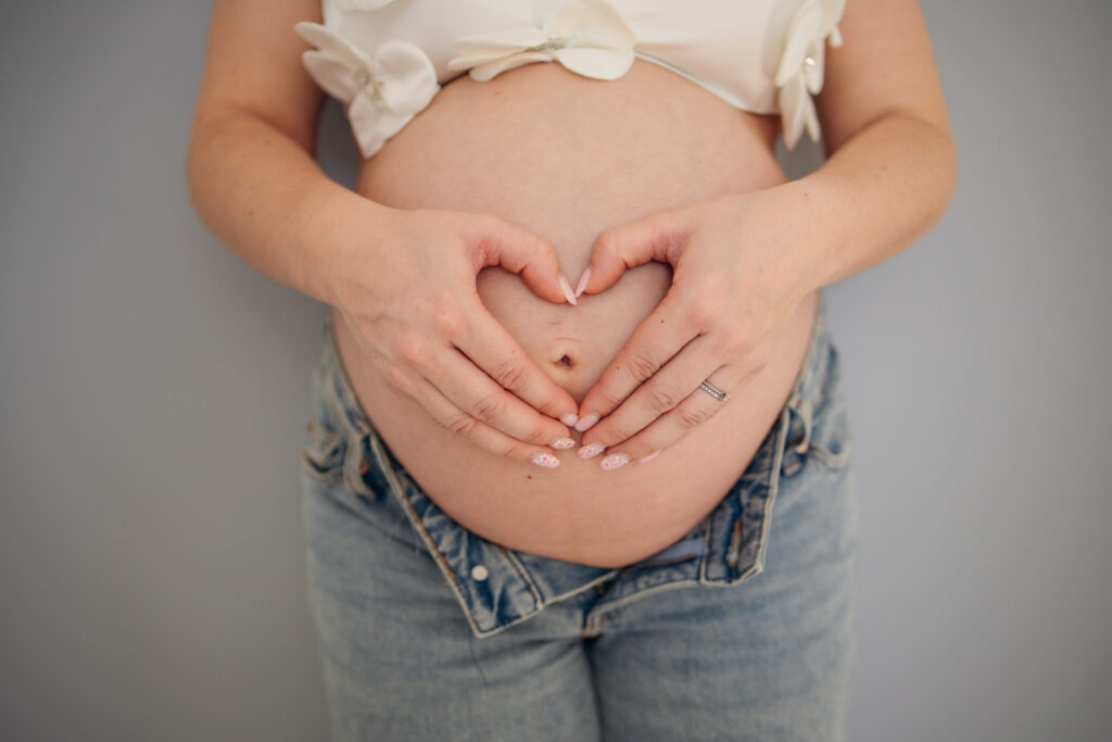 Babybauchshooting zu Hause Hände liegen als Herz auf dem Bauch