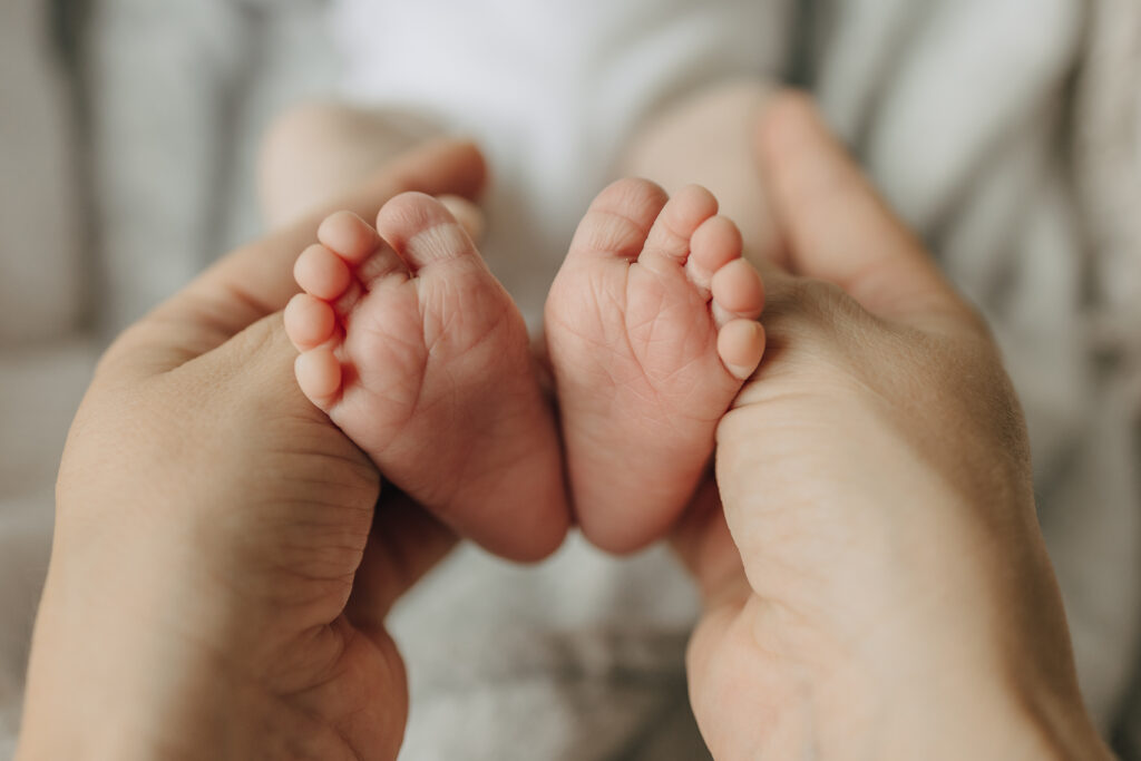 Neugeborenenshooting zu Hause in Lübeck. Die Mama hält die Füße von dem Baby in den Händen.